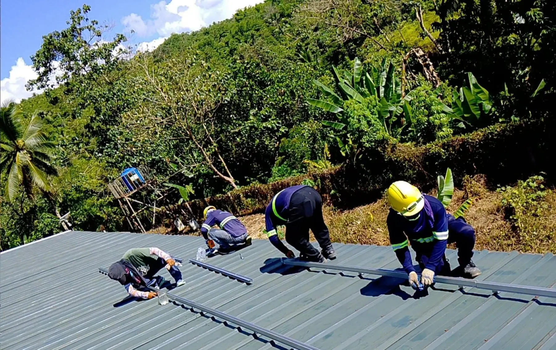 Solar installation crew working on a rooftop surrounded by trees