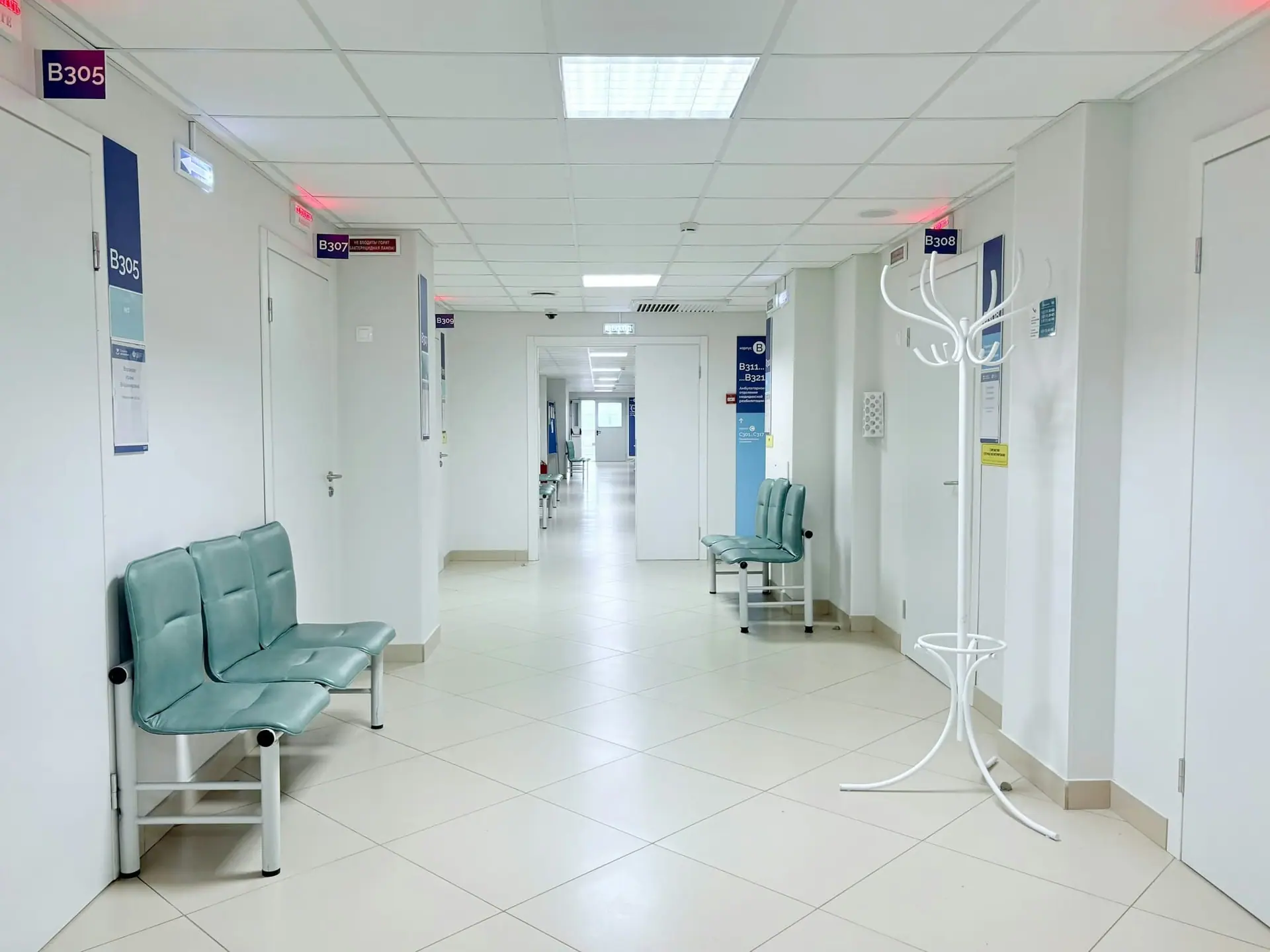 Clean, empty clinic corridor with waiting benches and consultation room doors
