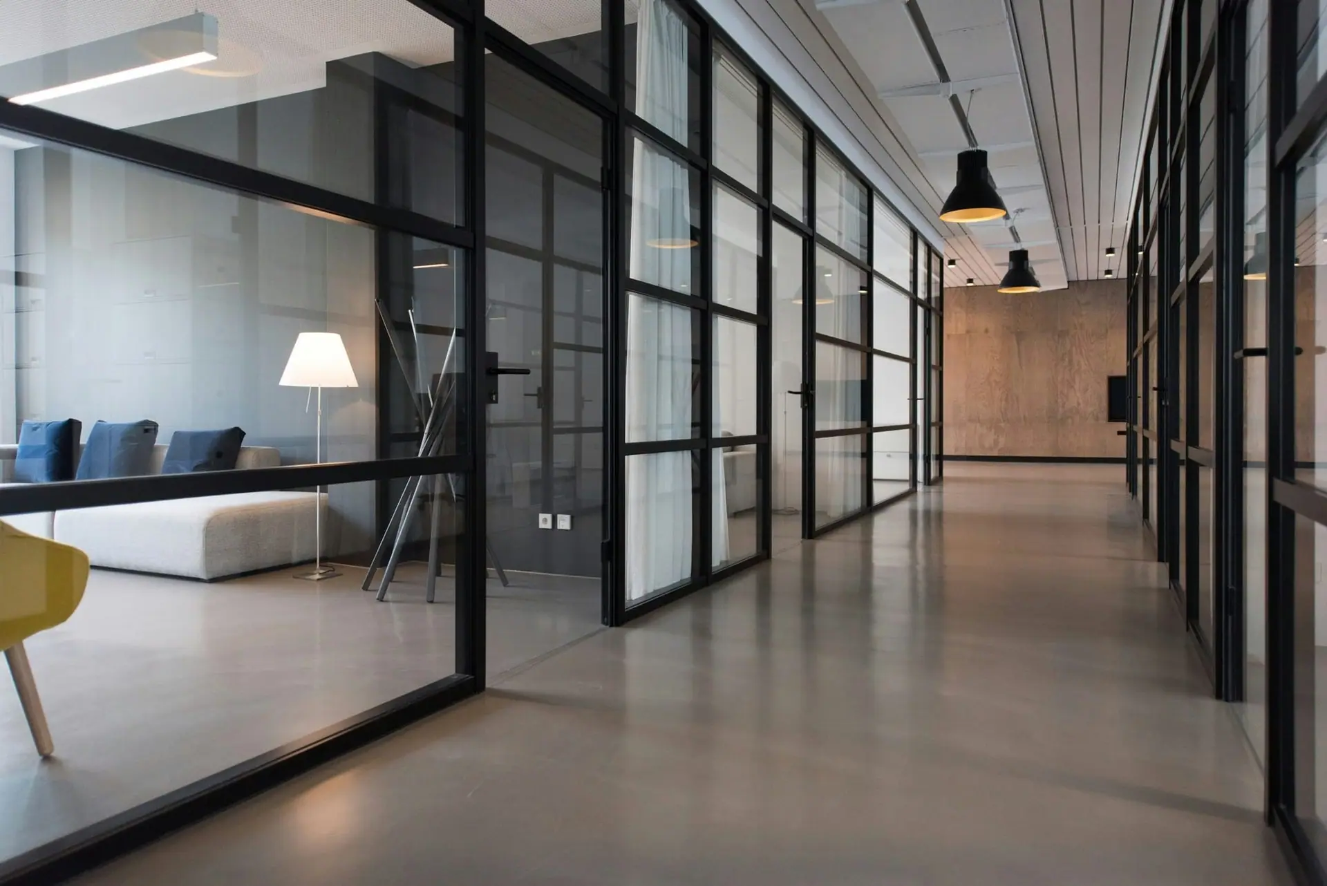 Modern office corridor lined with black-framed glass partitions and pendant lights