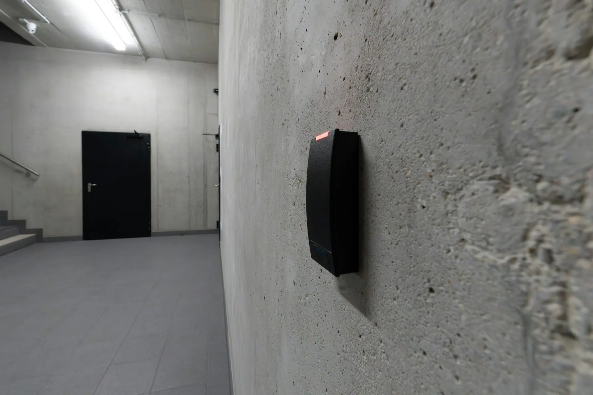 Access card reader with a red status light mounted on a concrete corridor wall
